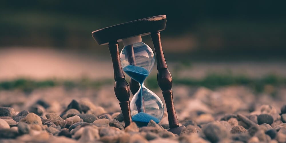 Eine Sanduhr steht schräg auf einem steinigen Untergrund.