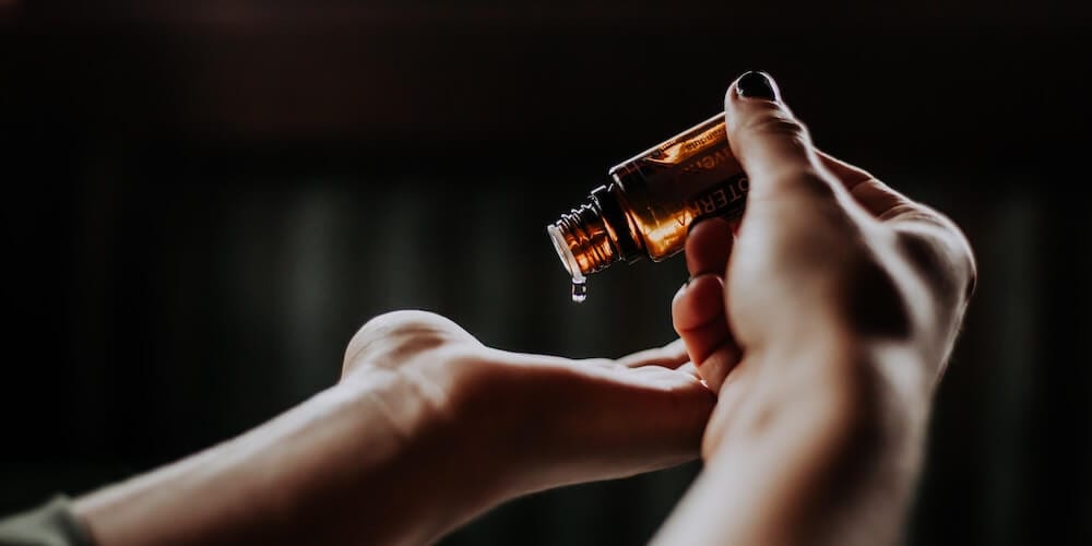 Eine Hand träufelt Flüssigkeit aus einer kleinen braunen Flasche auf den Arm.